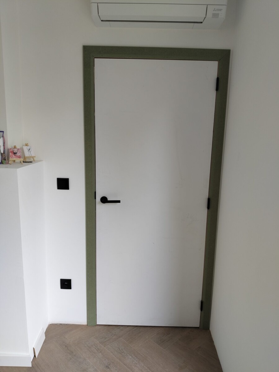 Witte binnendeur met groene omlijsting en zwarte klink Witte binnendeur met groene omlijsting en zwarte klink